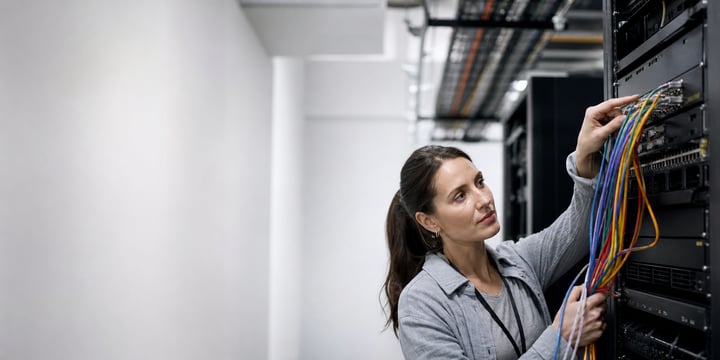 Network engineer plugging coloured patch cables into a rack of switches in a server room