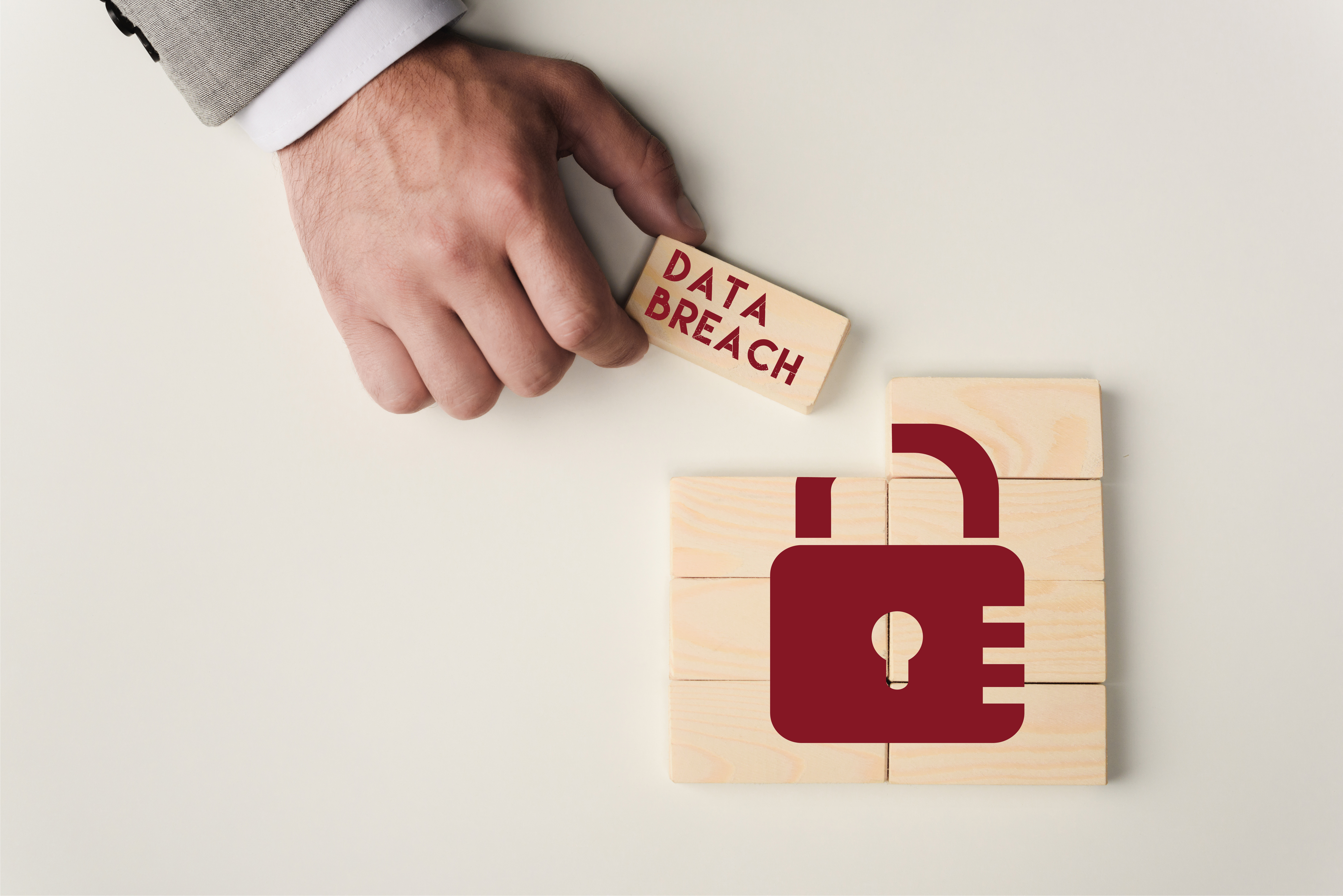 A hand placing a wooden “data breach” block next to a padlock icon to show a data breach investigation.